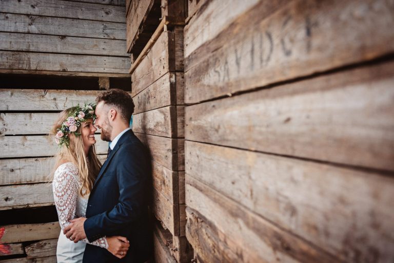 Rustic photo of bride and groom kissing amongst a load of wooden box's. Photo by Blooming Photography