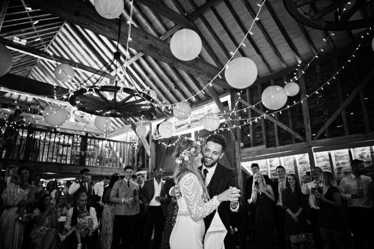 B&W Bride and groom dance, surrounded by their friends and family in a rustic barn called Over Barn, Gloucester. Candid photo by Blooming Photography