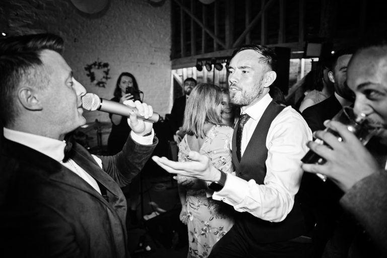 B&W photo of Chris Quidgley from the wedding band TuxFix singing in the crowd. Photo by Blooming Photography