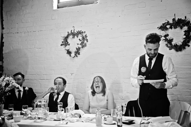 B&W photo of groom delivering his speech with his mum howling with laughter, funny photo by Blooming Photography.