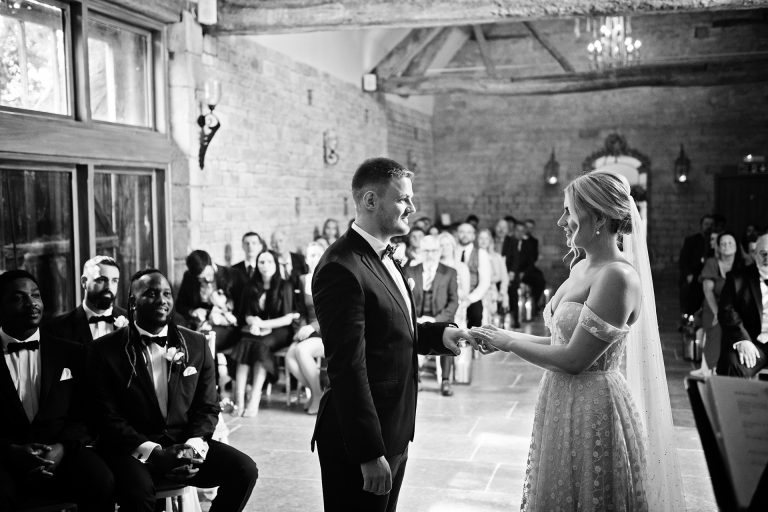 B&w image of a bride putting on the grooms wedding ring in a ceremony at Blackwell Grange.