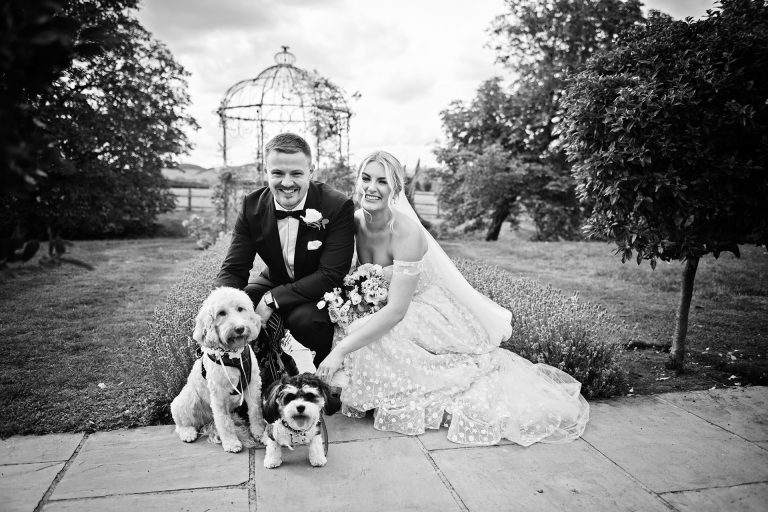B&w image of a bride and groom crouched down smiling next to their gorgeous small dogs. Candid wedding photo taken at Blackwell Grange.