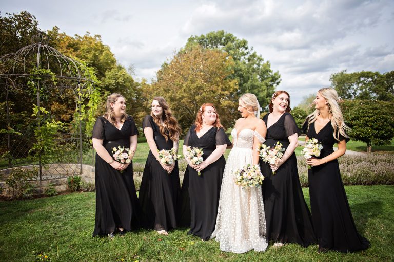 Bridesmaids in their black dresses, smile to the bride who is in her white dress. Looking autumnal at Blackwell Grange.