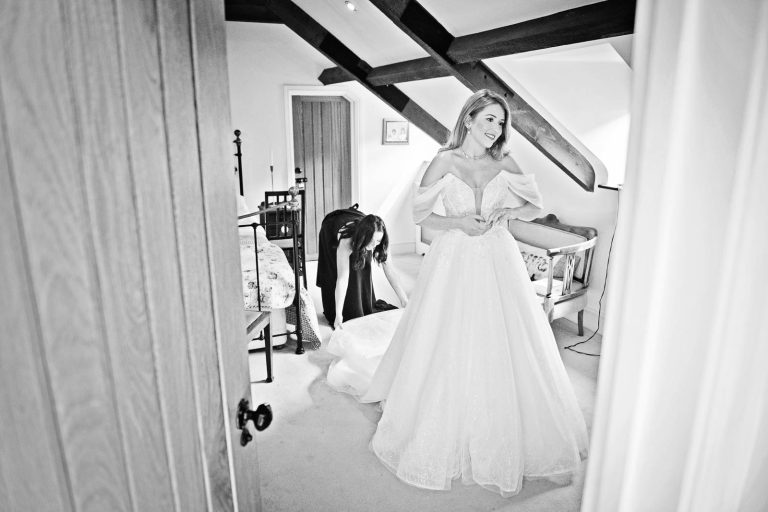 Black & white documentary photo of bride putting on her wedding dress.