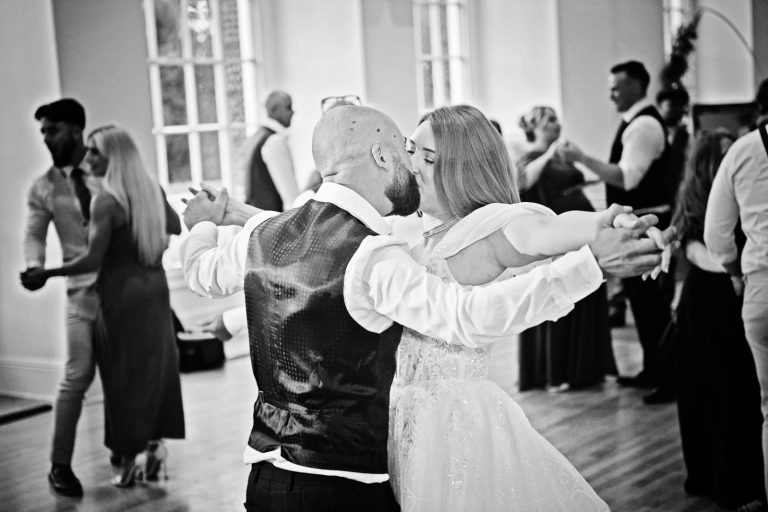 B&W photo of bride and groom dancing and kissing.
