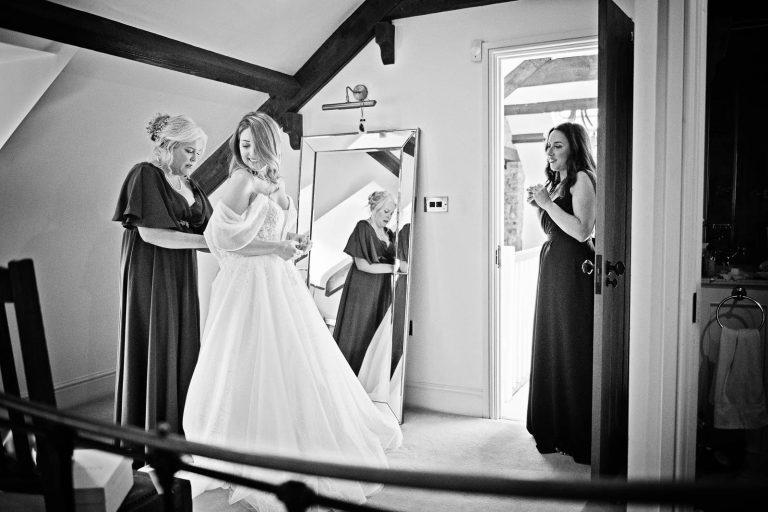 Black and white documentary photo of bride putting on her wedding dress.