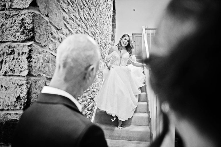 Bblack and white photo of bride walking down the stairs to be greeted by her dad. Cardiff wedding photographer, Blooming Photography