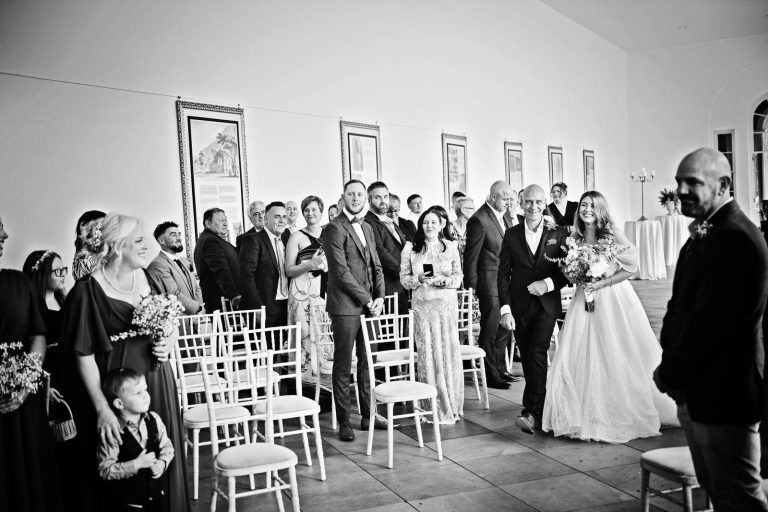 Relaxed B&W photo of a bride and her dad walking down the wedding isle at Margam Country Park..
