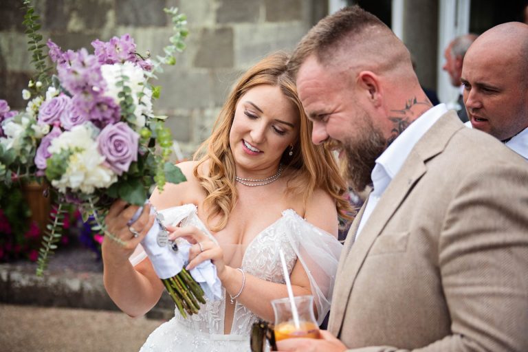 Photo taken of a bride talking to her brother and showing the details of a wedding bouquet at a wedding