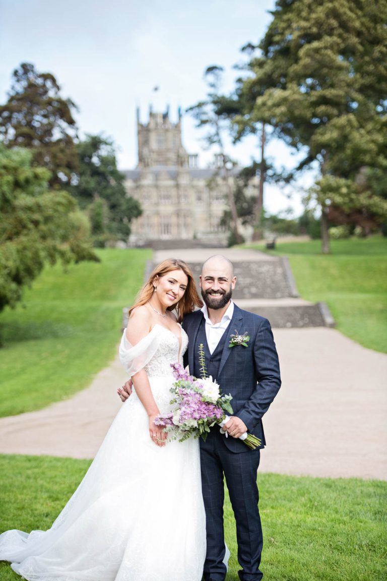 Wedding photo of bride and groom holding each other closely, smiling with Margam Country Park behind them.