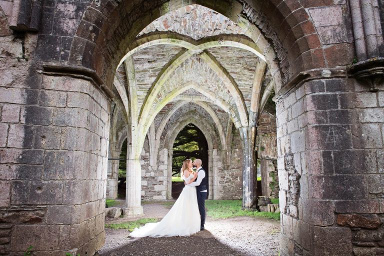 Amazing photo of bride and groom kissing under arches that are lit up.