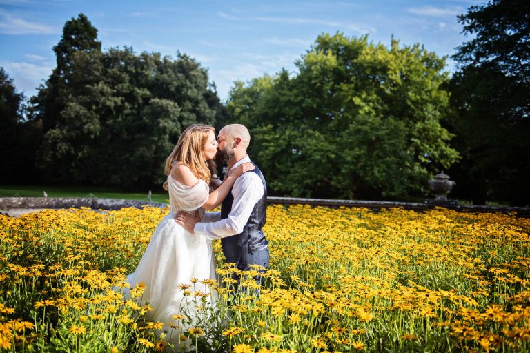 Natural wedding photograph of bride and groom kissing in a bank of yellow daisy flowers.