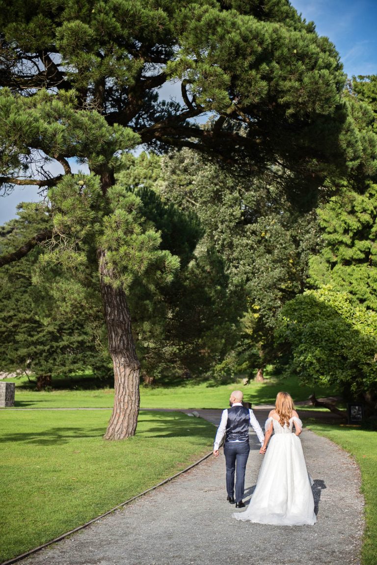 Relaxed wedding photography of bride and groom holding hands and walking away down a path at Margam Country Park.
