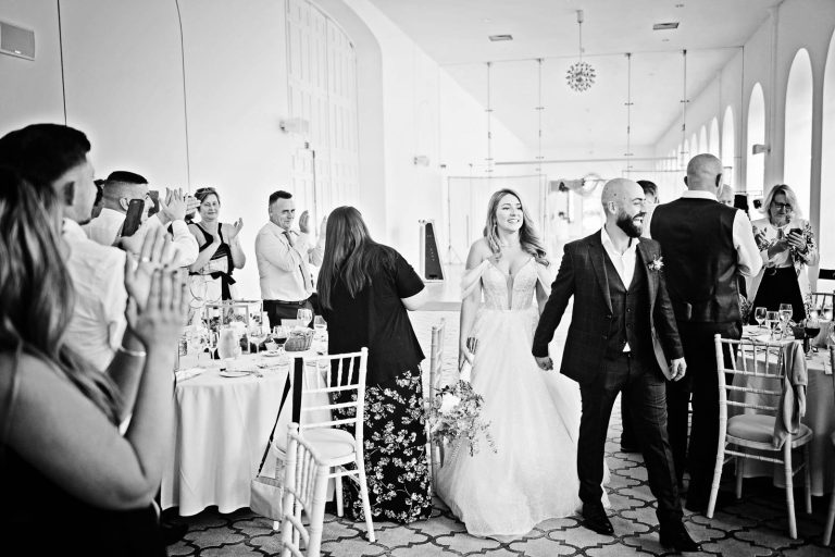 Natural image taken of the bride groom entering the wedding breakfast room cheered on by friends and family in The Orangery at Margam Country park