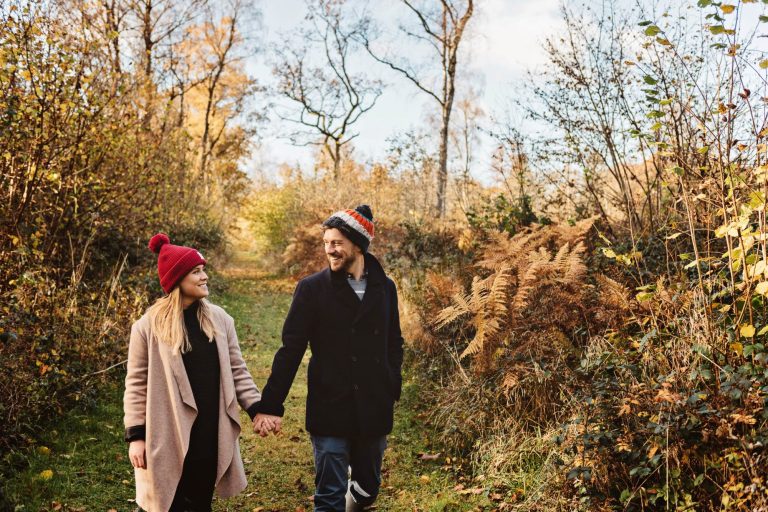 Couple hold hands as they walk in Westonbirt Arboretum for their engagement shoot.