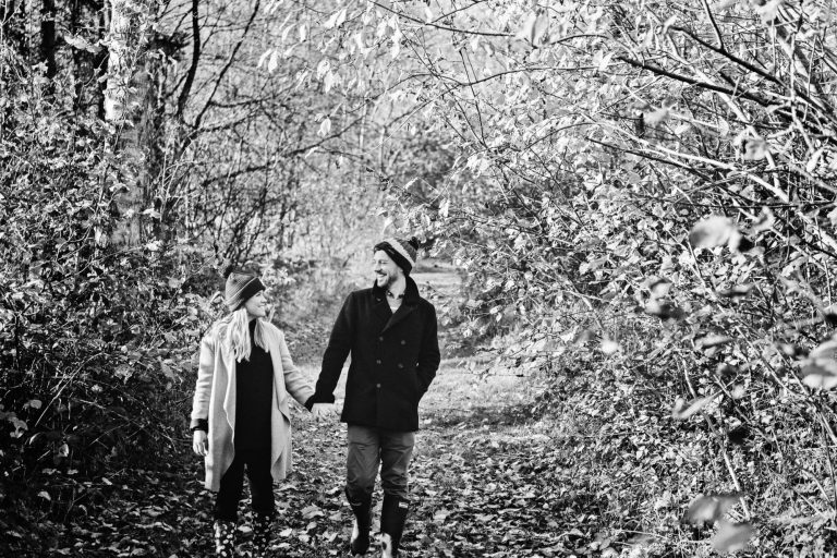 B&W photograph of a couple holding hands as they walk through a woodland path at Westonbirt Arboretum for their engagement shoot.