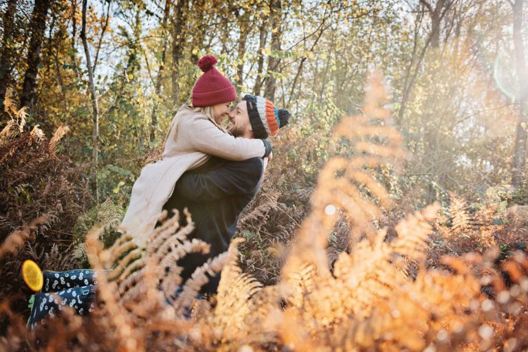 Autumnal setting with couple hugging and smiling taken at Westonbirt Arboretum for their engagement shoot.