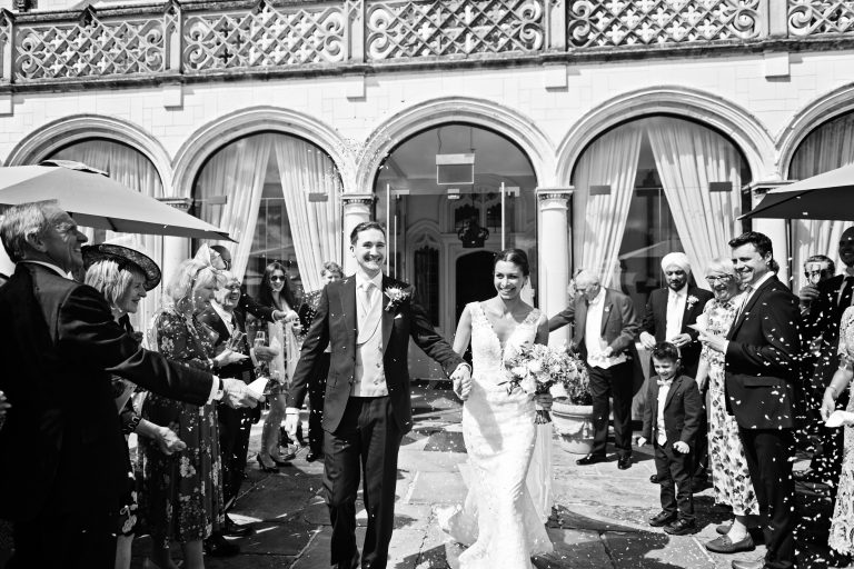 A timeless black and white photograph of the bride and groom walking down a confetti isle made by family and friends at Danesfield House Hotel and Spa.