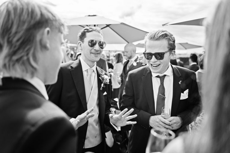 The groom and his groomsmen exchange stories and are laughing and smiling. Classic black and white image. Photographed at Danesfield House Hotel and Spa.