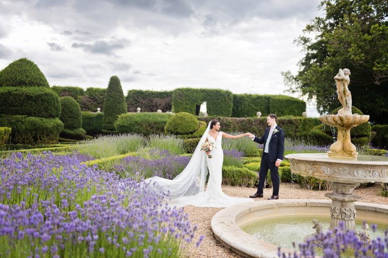 Bride and groom in the grounds at Danesfield House Hotel and Spa. Bride and groom hold hands behind the water fountain. Really elegant photograph.