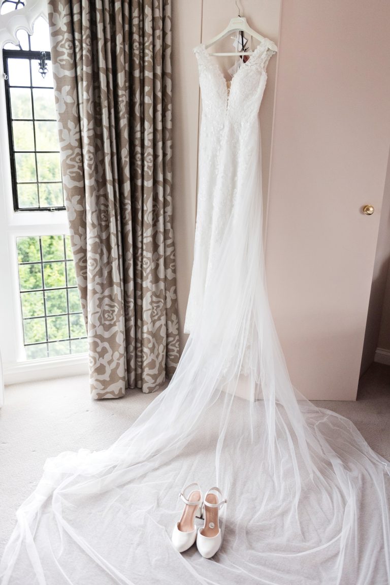 Wedding dress hung up with some wedding shoes laid on top of the train of the dress. Danesfield House Hotel and Spa.