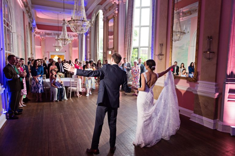 Bride and groom do their first choreographed dance. Backs facing, crowds reaction. Photographed in the elegant Danesfield House Hotel and Spa Ballroom.