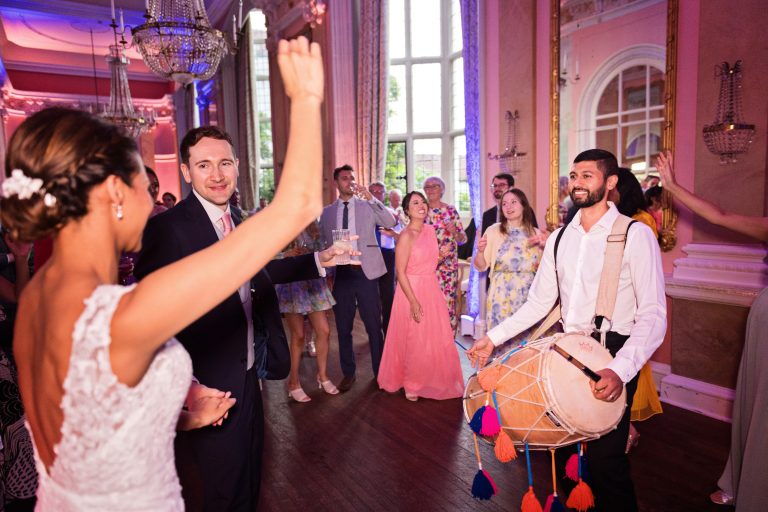 Bride and groom greet the Indian drummers. Photographed in the elegant Danesfield House Hotel and Spa Ballroom.