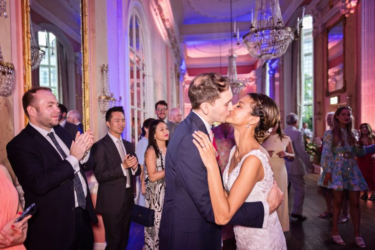 Bride and groom kiss to the applause of their guests. Photographed in the elegant Danesfield House Hotel and Spa Ballroom.