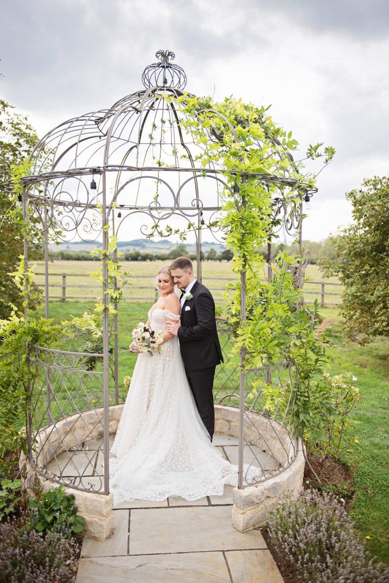 bride and groom embrace whilst they inside a metal arch
