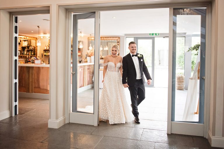 Bride and groom smiling as they enter the wedding breakfast room. Photo by Blooming Photography. Taken at Blackwell Grange, Warwickshire.