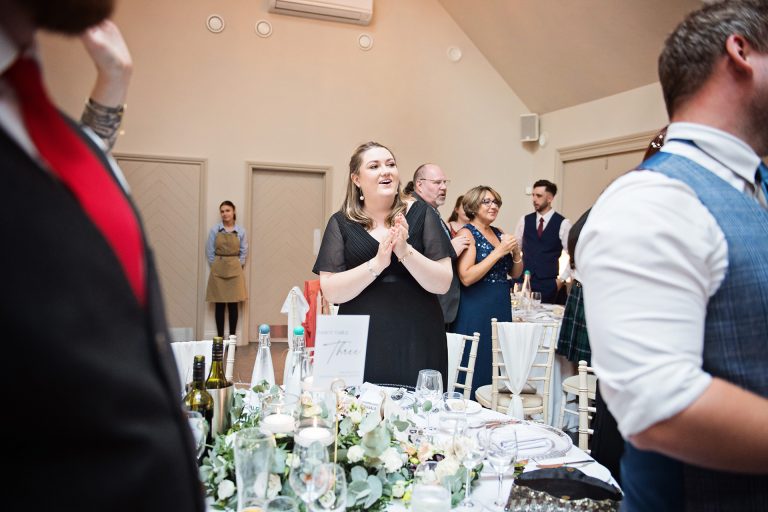 Candid photo by Blooming Photography. Taken at Blackwell Grange, Warwickshire. Image of wedding guests smiling and clapping as the bride and groom enters the wedding breakfast.