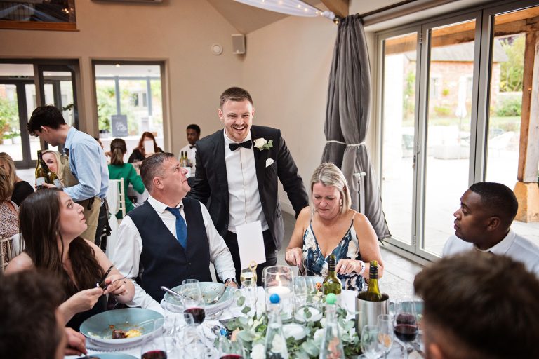 Groom smiling as he talks to his guests during the wedding breakfast. Candid photo by Blooming Photography. Taken at Blackwell Grange, Warwickshire.