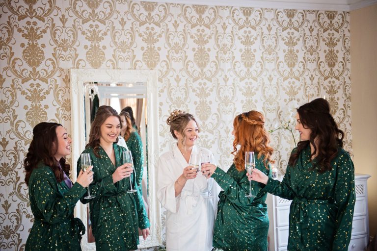 Brides in their wedding gowns cheering to each other with a glass of fizz. Photographed at Eastington Park Winter Wedding by Blooming Photography