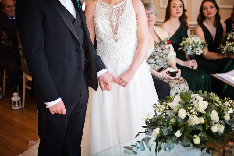 Close up photo of bride and groom tentatively holding hands during the wedding ceremony.