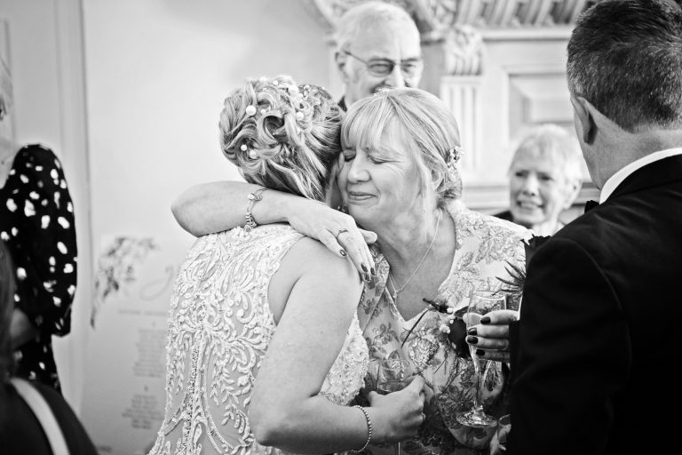 Candid photograph of mother of the groom hugging the bride at Eastington Park
