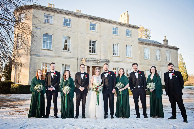 Wedding party, standing in a line on snow with Eastington Park behind them. Looks beautiful.