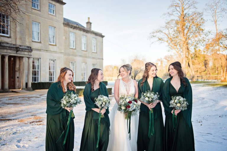 Bride and bridesmaids standing in a line on snow with Eastington Park behind them. Looks beautiful.