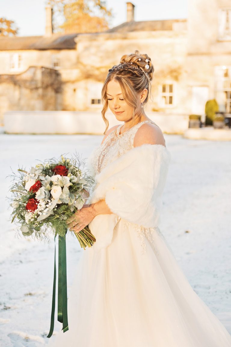 A bride holding her wedding bouquet with snow and Eastington Park behind them.