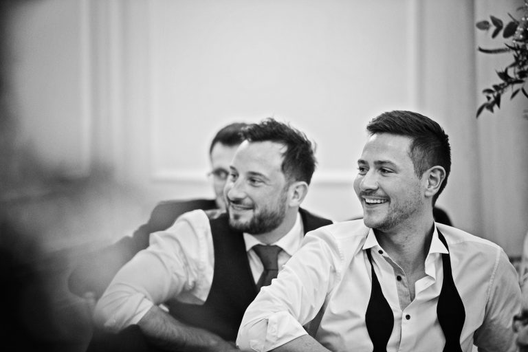 Guests laugh at a wedding speech. Black and white photograph by Blooming Photography taken at Eastington Park at Christmas Wedding.