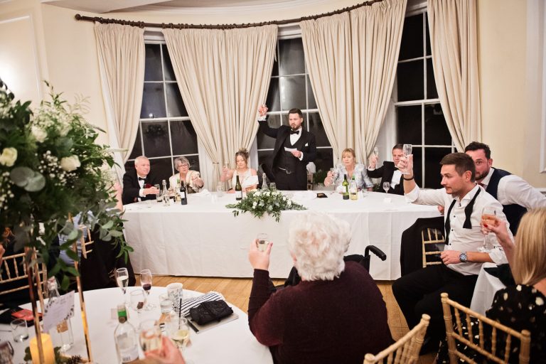 Wide view of groom raising his glass to signal the end of his speech. Photograph by Blooming Photography taken at Eastington Park at Christmas Wedding.