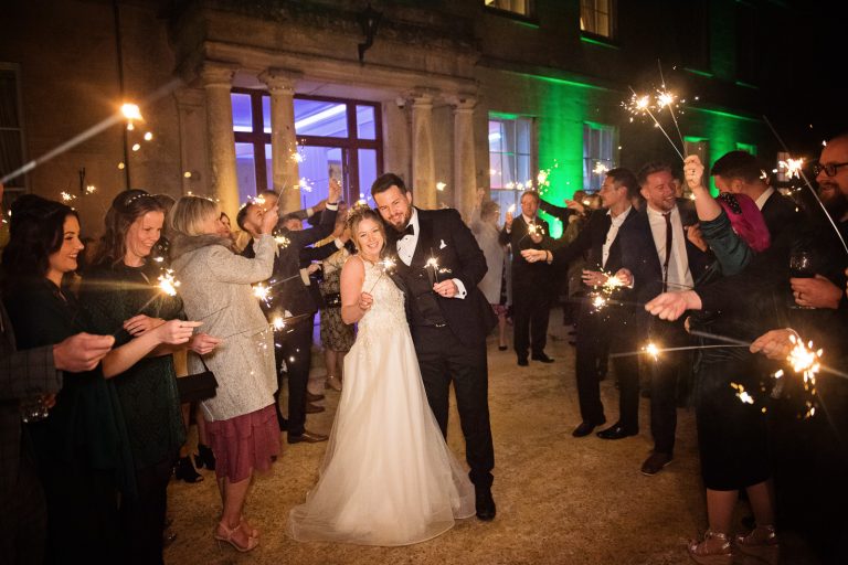 Bride and groom hug with their friends and family outside with sparklers. Taken at Eastington Park at Christmas Wedding.