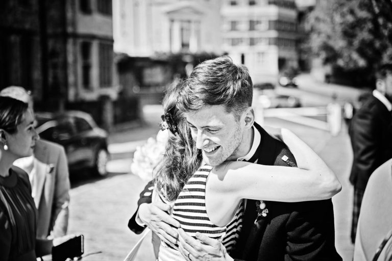 Groom hugging outside Winchester Registry office wedding. Candid black & white photo by Blooming Photography
