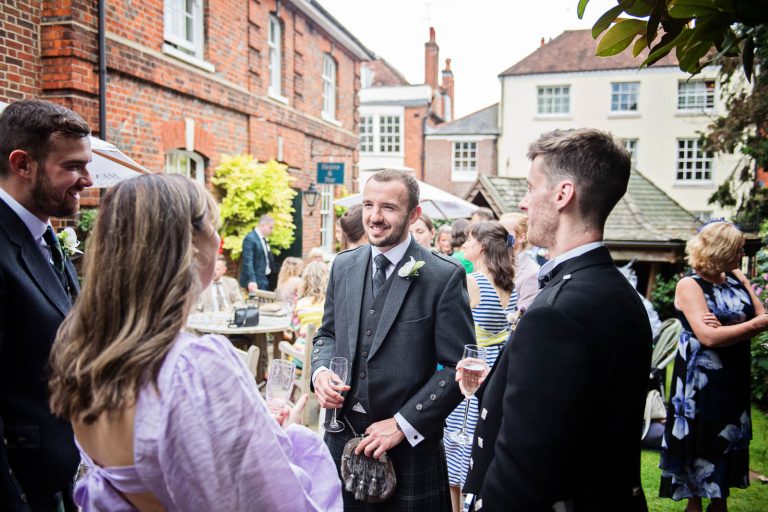 Candid wedding photo of guests talking to groom at Hotel Du Vin Winchester, photo by Blooming Photography