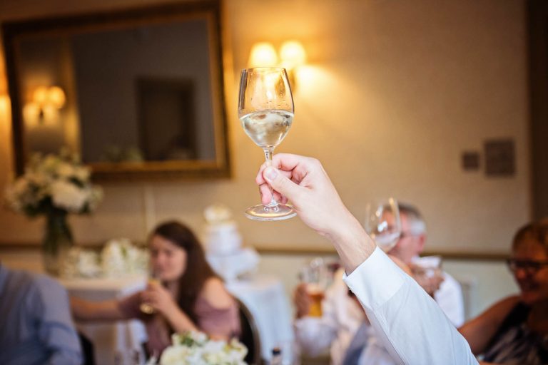 Toast the speeches, glass being held up in the air at Hotel Du Vin Winchester for a wedding. Photo by Blooming Photography.