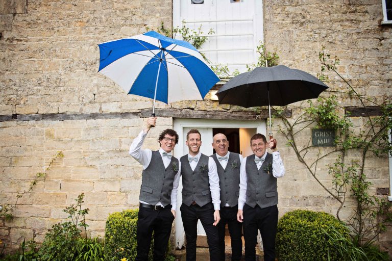 Groomsmen holding their umbrellas up during the rain.