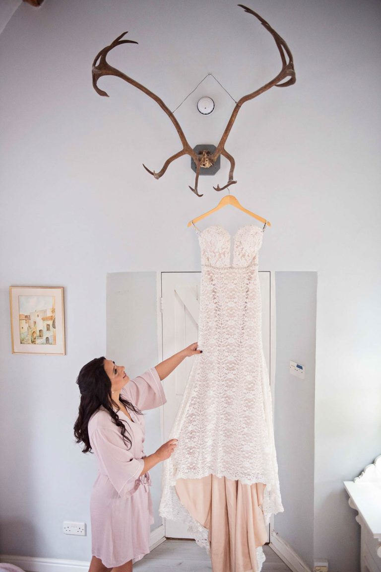 Brides dress hung up with the bridemaid looking up at it.