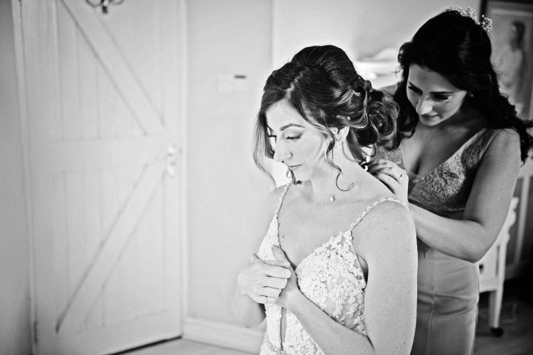 B&W photo of sister of the bride doing the brides wedding dress up.