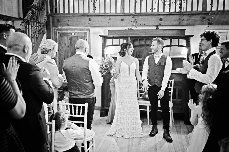 B&W photo of bride and groom getting congratulated by their friends and family at their end of their wedding ceremony at Owlpen Manor.