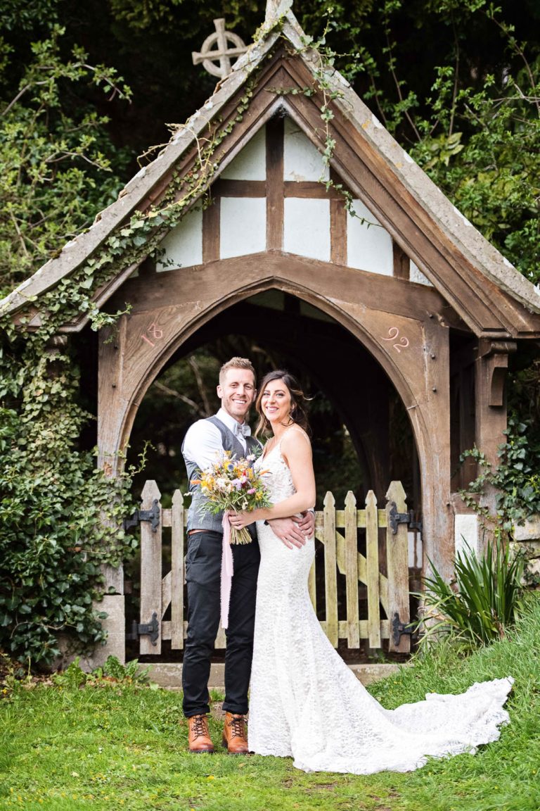 Bride and groom stand in front of a church arch.