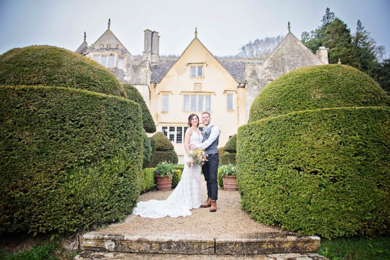 Bride and groom stand with Owlpen Manor behind them.